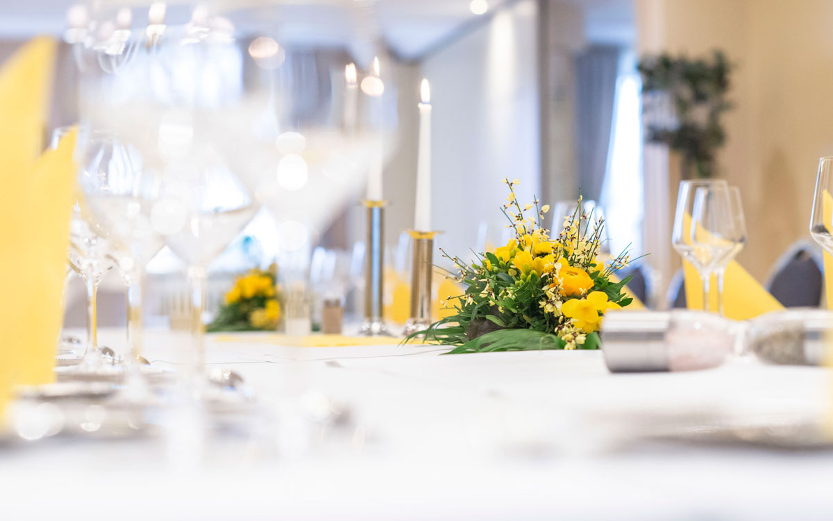 Detailaufnahme eines gedeckten Tisches mit gelben Gestecken für ein Geburtstag / Jubiläum im Hotel Hennies Haupthaus.