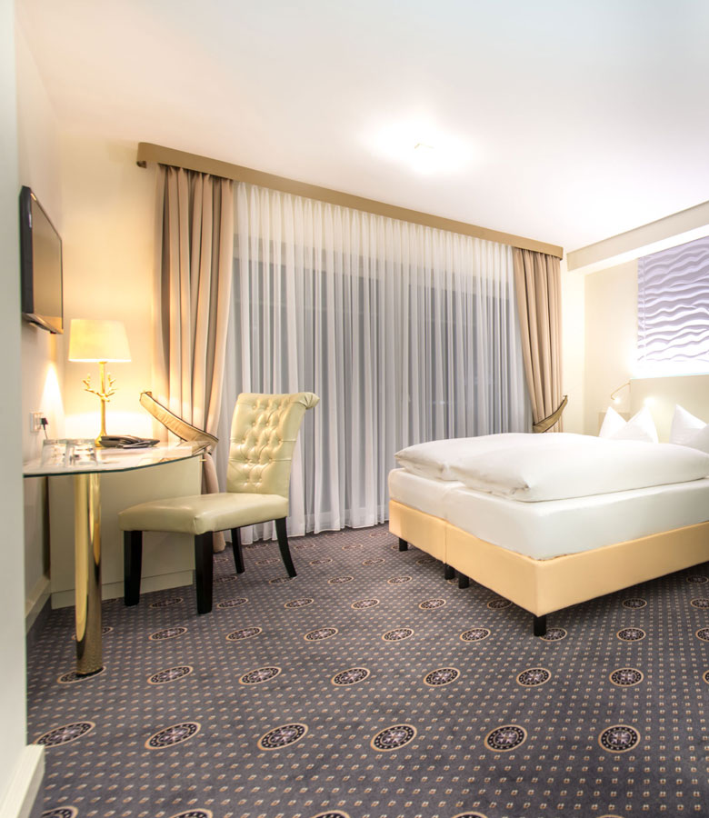 Einblick in ein Doppelzimmer im Hotel Hennies ausgestattet mit einem Bett und Schreibtisch.