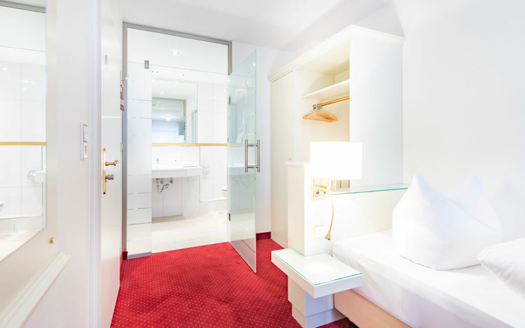 Einblick in ein modernes Einzelbettzimmer im Hotel Hennies mit Blick in das separate Badezimmer.